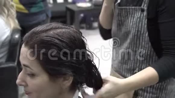 理发师发型师梳湿发梳东方女孩谁坐在理发店和准备理发头发护理视频的预览图
