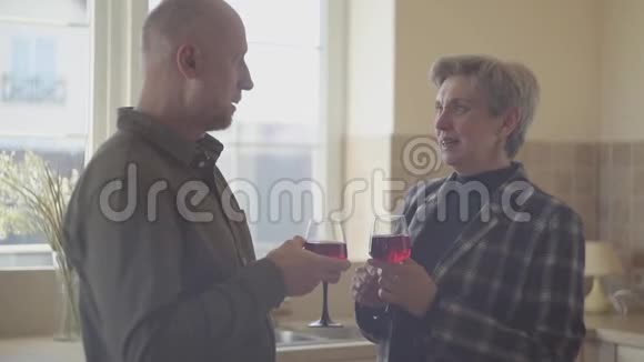 一对戴着酒杯的老夫妇站在厨房的宽窗旁家庭关系视频的预览图