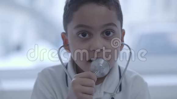 一幅可爱的小男孩的肖像他的耳朵里有听诊器在镜头里看着在设备里呼吸保健健康视频的预览图