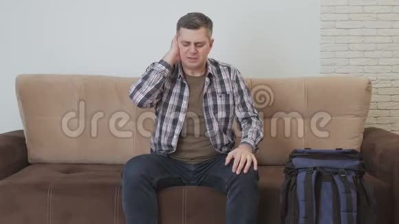 一个中年男人坐在沙发上耳朵疼沙发旁边是一个大型旅游背包视频的预览图
