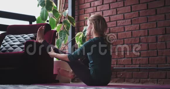 女士在家里在她放松的空间练习瑜伽她伸展腿和身体以获得更多的能量一整天现代视频的预览图