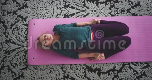 伸展身体的女士早上在家里做瑜伽运动她坐在粉红色的垫子里健康的生活方式视频的预览图