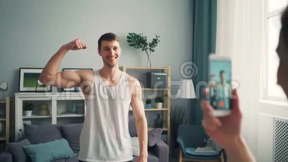 性格开朗的运动员摆出智能手机摄像头显示肌肉视频的预览图