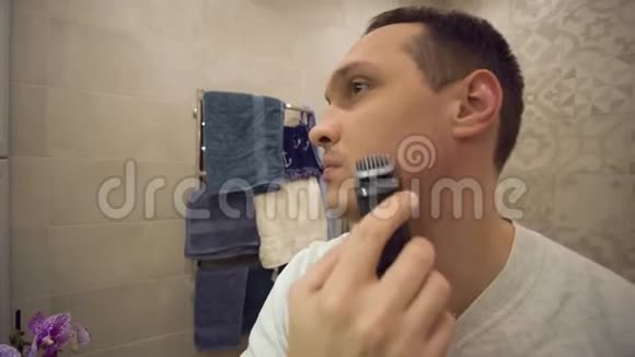 男卫生带电动剃须刀的年轻人照镜子在浴室里刮胡子视频的预览图