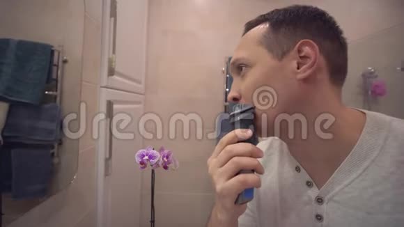 男性美容护理的常规生活方式成年男性用电动剃须刀将胡须剃在洗手间镜子前视频的预览图