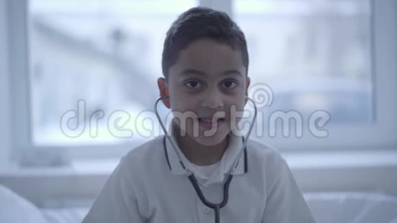 可爱的小男孩的肖像耳朵里有听诊器微笑着看着镜头保健健康生活方式和视频的预览图