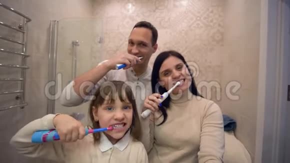 家庭刷牙可爱的小女孩带着父母在镜子前刷牙视频的预览图