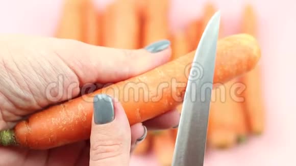 用刀子在粉红色背景下剥胡萝卜的过程视频的预览图