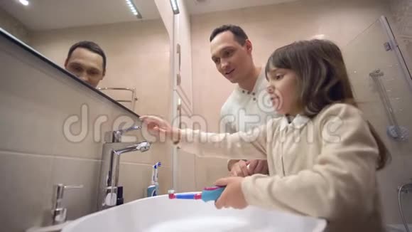 幼儿晨间卫生小父亲在镜子前教女儿刷牙和监测口腔健康视频的预览图
