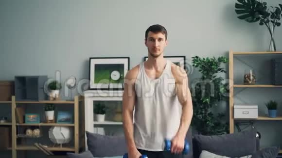 英俊的运动员用哑铃举起手臂在家里练习视频的预览图