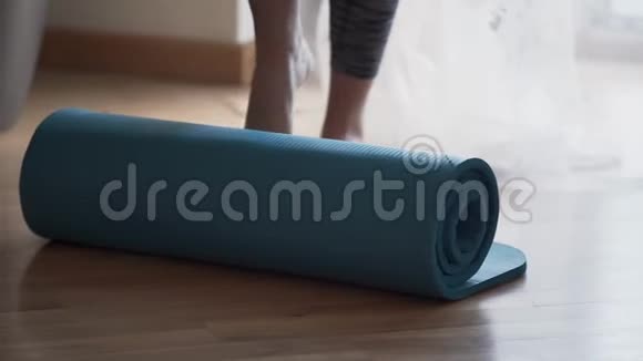 不认识的女人用她的脚打开躺在地板上的瑜伽垫准备瑜伽课程的女孩视频的预览图