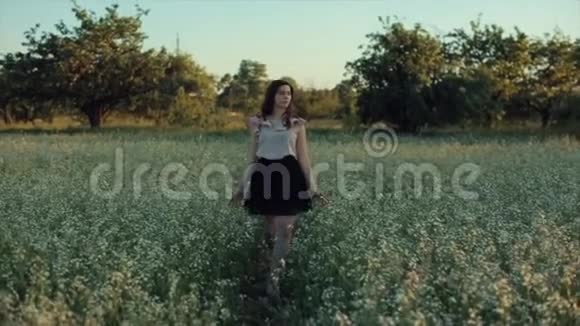 美丽的年轻黑发女孩穿着黑色裙子走在田野上摆在镜头前触摸头发视频的预览图