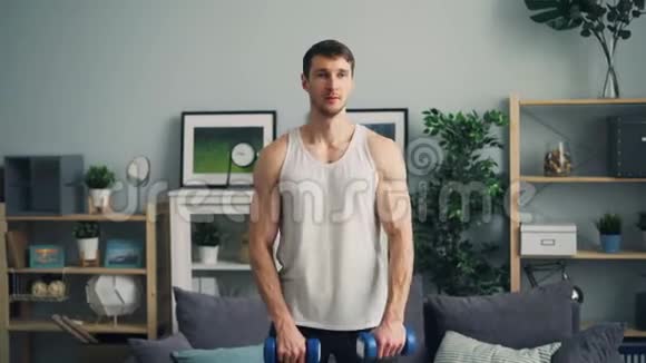 肌肉男训练在公寓里用沉重的哑铃举起手臂呼吸视频的预览图