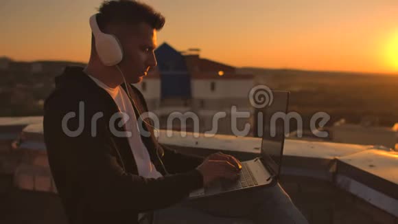 日落时分一个戴着耳机的自由职业者站在屋顶上写着键盘代码页小生意听着听着视频的预览图