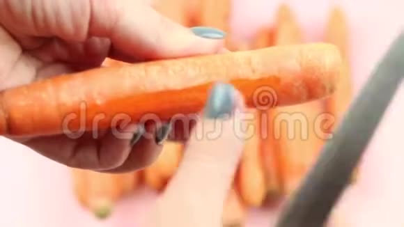 用刀子在粉红色背景下剥胡萝卜的过程视频的预览图