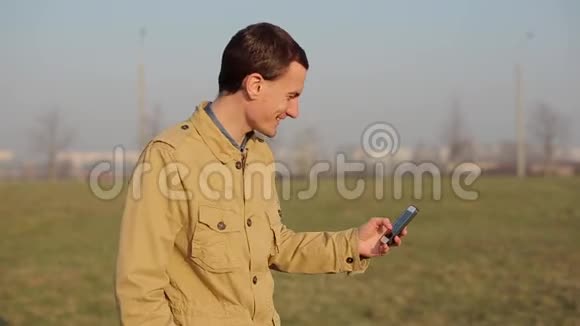 快乐的红发白种人使用一个智能手机在公园的背景树并制作一个自拍日出或日落视频的预览图