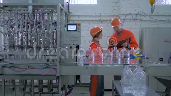 在塑料装瓶矿泉水输送线附近戴安全帽盖帽的行业工人视频的预览图
