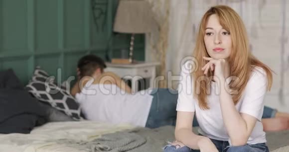 年轻的女人担心关系中的问题坐在床上她的男朋友正躺在附近转身离开视频的预览图