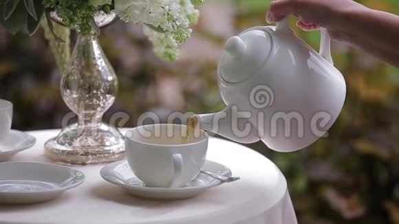 女人的手在把热茶倒进一个白色的杯子里快关门盛满茶杯的白桌上摆着一个装饰着视频的预览图