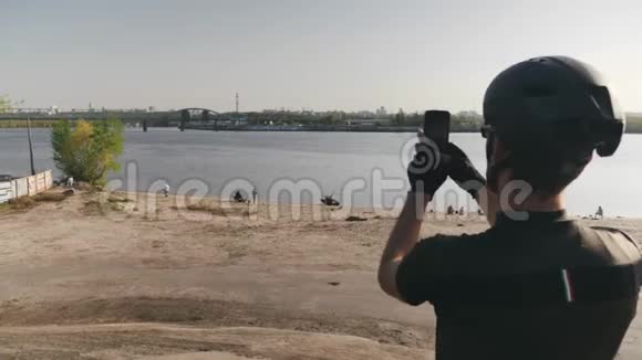 男性骑自行车的人拿着手机相机拍摄河流桥梁和城市的照片一个骑自行车的人拿着手机拍照视频的预览图