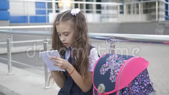 在学校大楼附近穿校服的女孩放学后在笔记本上写一些东西视频的预览图