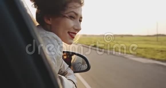 美丽的女孩把手伸出车窗外在阳光明媚的天气里微笑慢动作视频的预览图