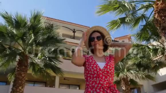 年轻快乐的女人摆着红色的裙子和太阳镜镜头旋转的女人摆姿势蓝天和棕榈树在巴视频的预览图
