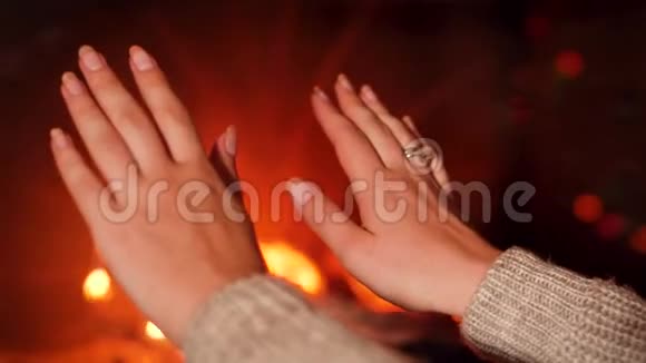 在壁炉里燃烧着火一个年轻女子用手暖和着视频的预览图