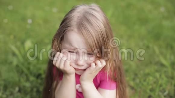 美丽可爱的小女孩在草地上哭泣被绿草包围中等特写镜头视频的预览图