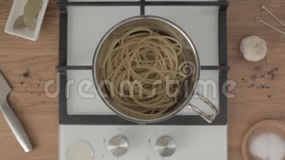 手把半勺油放在金属锅里煤气炉上放着煮好的意大利面视频的预览图