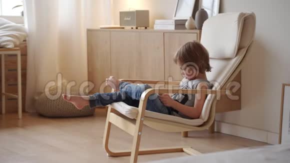 可爱的5岁白种人男孩坐在Armchar和使用平板电脑在轻型房间视频的预览图