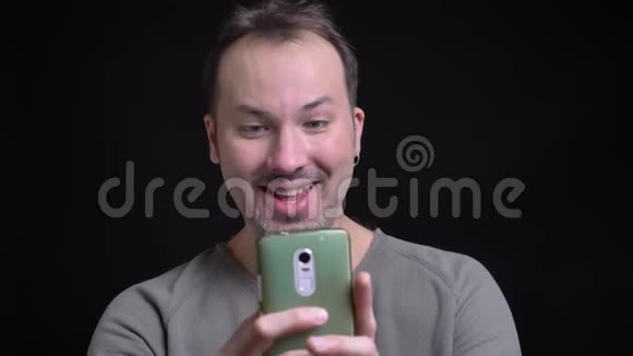 中年白种人的肖像带耳环用智能手机在黑色上制作滑稽的自拍照片视频的预览图