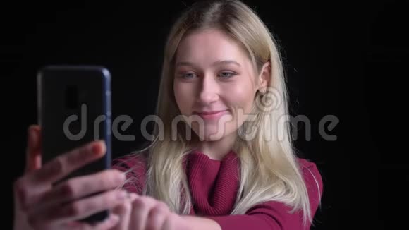 一位年轻漂亮的白种人女性的特写镜头她在电话里打着视频微笑着用手打招呼视频的预览图