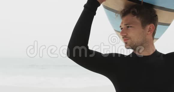 高加索男性冲浪者在海滩头顶着冲浪板的正面景色视频的预览图