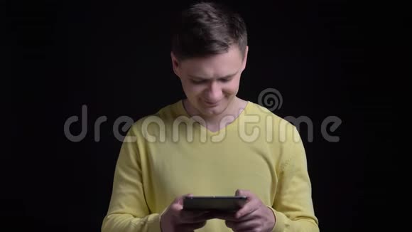 穿着黄色毛衣的中年白人男子看着平板电脑在黑色背景下对着镜头微笑视频的预览图