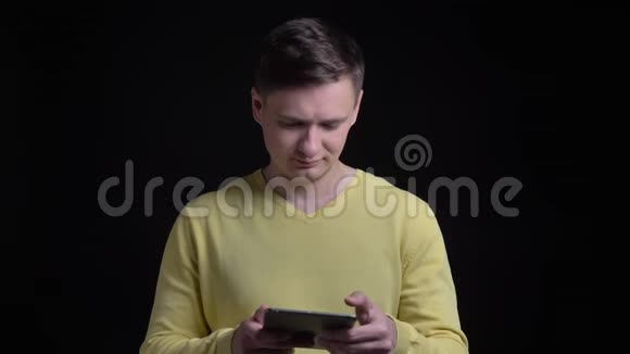 中年白种人穿着黄色毛衣和平板电脑一起工作在黑色背景下平静地看着镜头视频的预览图