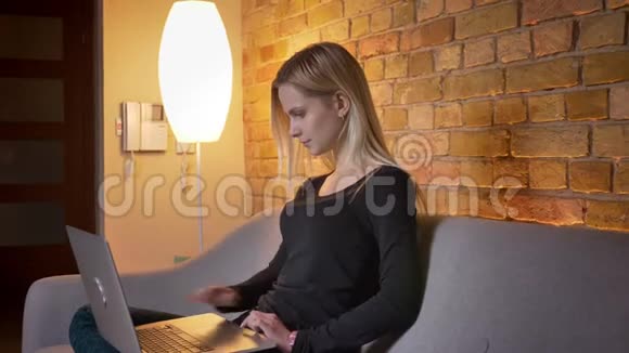 特写侧景照片年轻漂亮的金发女性使用笔记本电脑坐在室内沙发上视频的预览图