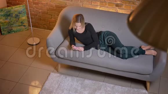 年轻少女使用手机躺在沙发上舒适的家中休息的特写镜头视频的预览图
