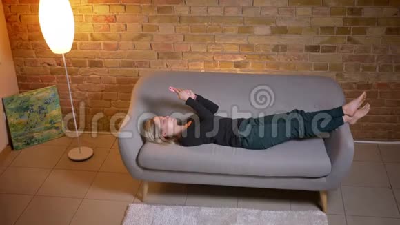 年轻女学生使用手机躺在舒适的家中躺在沙发上的特写镜头视频的预览图