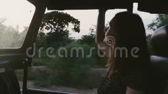 年轻快乐美丽的女游客微笑着在日落森林的游览车上享受大气的狩猎之旅视频的预览图
