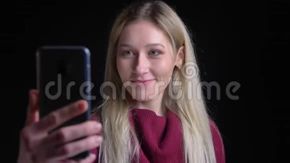 一个年轻漂亮的白种人女孩的特写镜头她留着一头长长的金发在视频中打着微笑挥手问好视频的预览图