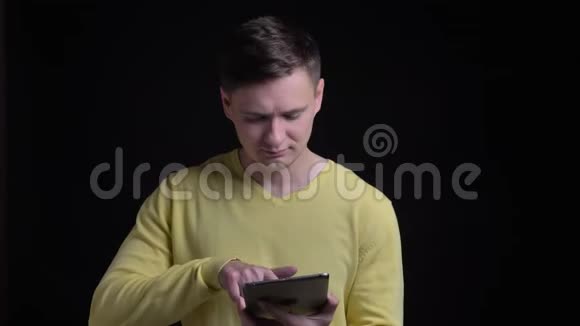 中年白种人穿着黄色毛衣在黑色背景上微笑地把平板电脑的蓝色屏幕变成相机视频的预览图