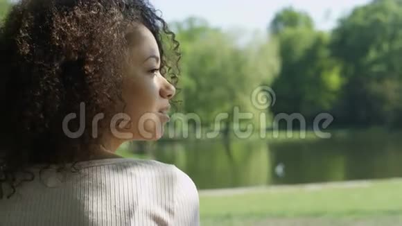 年轻美丽的混血女人卷发在一个绿色的公园里快乐地微笑视频的预览图