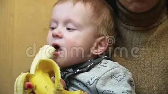 小男孩在妈妈的帮助下吃香蕉她坐在膝盖上视频的预览图