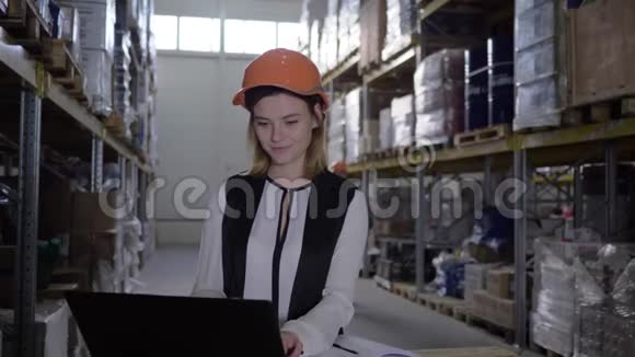 戴头盔的工人与仓库工人交谈同时在货架之间使用笔记本电脑视频的预览图