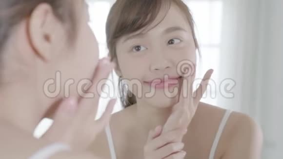 美丽的年轻亚洲女性快乐地将面霜或乳液与保湿剂一起涂抹在皮肤上视频的预览图