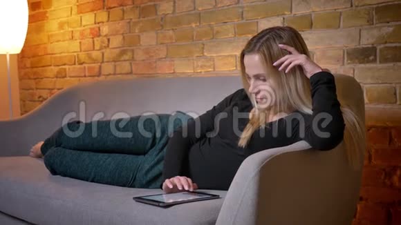 年轻漂亮家庭主妇使用平板电脑躺在沙发上悠闲地躺在舒适的家里视频的预览图