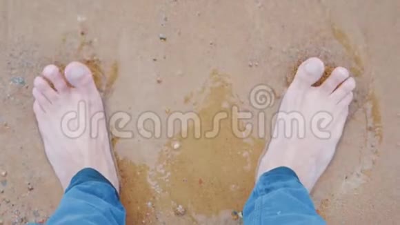 海浪冲刷着穿着牛仔裤的男人在白沙上的脚视频的预览图