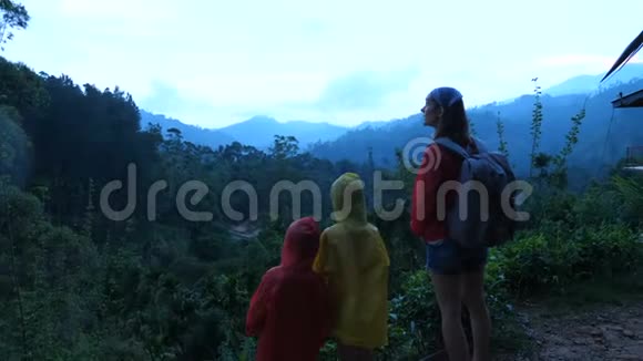 快乐的年轻妈妈带着两个小朋友徒步旅行在雨天观看异国情调的热带森林山脉景观视频的预览图