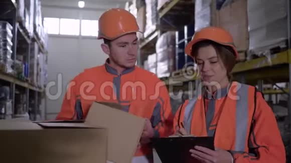 两名员工穿着工作服戴着头盔在仓库附近的箱子里讨论工作视频的预览图